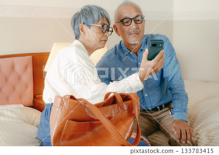 一對老年夫婦在飯店一邊看智慧型手機一邊聊天。 133783415