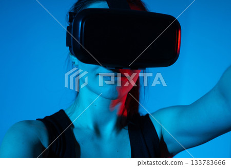 Woman interacting with virtual reality headset illuminated by dramatic blue and red futuristic light Woman interacting with virtual reality headset illuminated by dramatic blue and red futuristic light 133783666