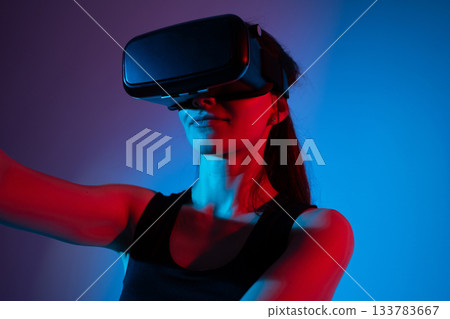 A female engineer researches VR technology in a neon environment, exploring virtual interfaces 133783667