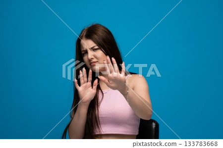 Young woman expressing disgust and discomfort with defensive hand gesture on vibrant blue studio background Young woman expressing disgust and discomfort with defensive hand gesture on vibrant blue studio background 133783668