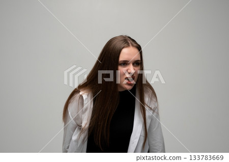 Young woman leaning forward with angry aggressive facial expression in minimalist studio portrait Young woman leaning forward with angry aggressive facial expression in minimalist studio portrait 133783669