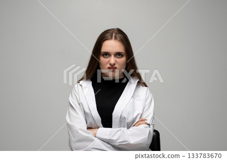 Young woman expressing anger with crossed arms and intense facial expression in studio portrait Young woman expressing anger with crossed arms and intense facial expression in studio portrait 133783670
