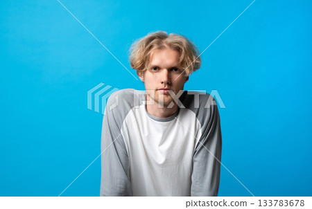 Thoughtful young man leaning slightly forward with serious expression on bright blue background Thoughtful young man leaning slightly forward with serious expression on bright blue background 133783678