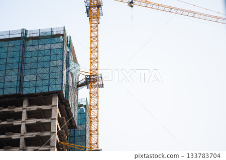 Tower crane and modern skyscraper construction site under clear blue sky in daylight Tower crane and modern skyscraper construction site under clear blue sky in daylight 133783704