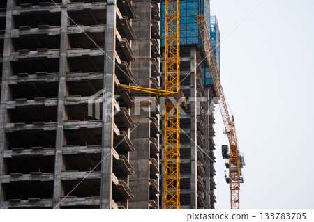 High rise concrete building construction with yellow crane and unfinished structure under blue sky High rise concrete building construction with yellow crane and unfinished structure under blue sky 133783705