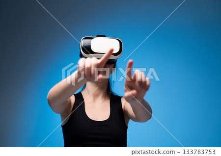 Woman interacting with virtual reality interface using VR headset in bright studio with blue background lighting Woman interacting with virtual reality interface using VR headset in bright studio with blue background lighting 133783753