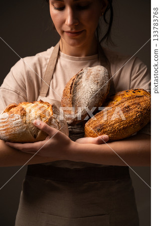 A female baker holds several handcrafted artisan loaves with crackled crusts and textured surfaces 133783768