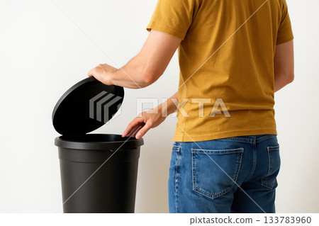 A man opens the lid of a black trash can. 133783960