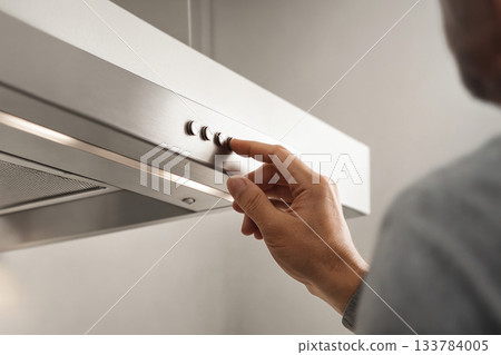 The man turns on the kitchen hood by pressing a button. The man turns on the kitchen hood by pressing a button. 133784005