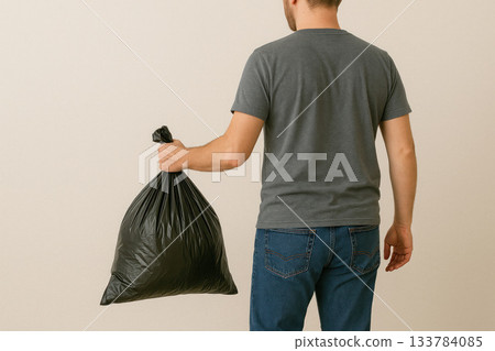 The man is holding a large black garbage bag in his hand. Space for text. The man is holding a large black garbage bag in his hand. Space for text. 133784085