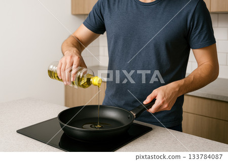A man pours vegetable oil into a pan in the kitchen. Space for text. A man pours vegetable oil into a pan in the kitchen. Space for text. 133784087
