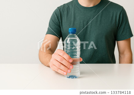 A man holds a bottle of clean drinking water on the table. Space for text. 133784118