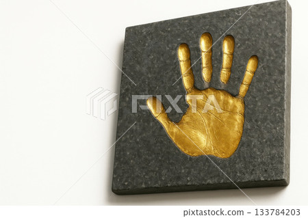 A golden palm print on a dark stone slab. Space for text. 133784203