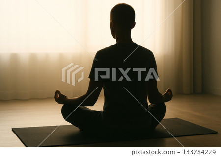 A man meditates in the lotus position in a quiet room. A man meditates in the lotus position in a quiet room. 133784229