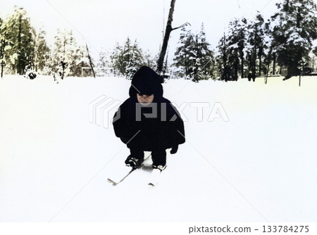 A vintage portrait of a little boy in a fur coat and hat learning to cross-country ski. Retro photo from the 1970s. A vintage portrait of a little boy in a fur coat and hat learning to cross-country ski. Retro photo from the 1970s. 133784275