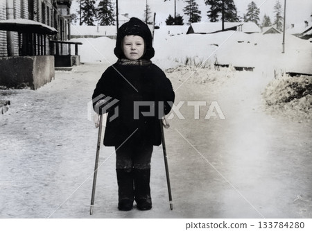 A vintage portrait of a little boy in a fur coat and hat learning to cross-country ski. Retro photo from the 1970s. A vintage portrait of a little boy in a fur coat and hat learning to cross-country ski. Retro photo from the 1970s. 133784280