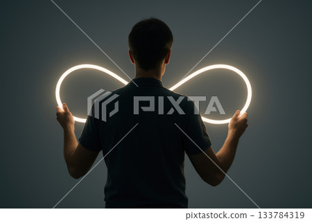 A person holds a luminous loop in the shape of an infinity symbol. 133784319