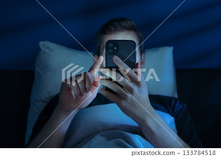 Man holds his smartphone close to face while brousing social media at night 133784518