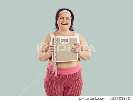 Happy overweight woman in sportswear holding bathroom scale Happy overweight woman in sportswear holding bathroom scale 133785588