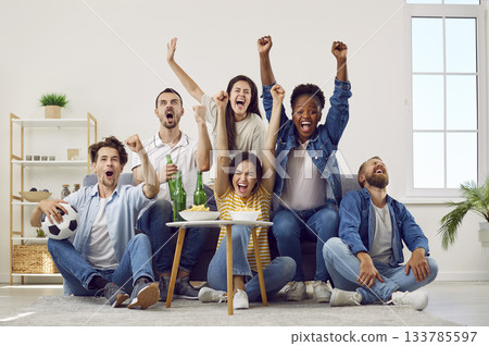 Happy excited diverse friends sitting on couch, watching soccer on TV and screaming Happy excited diverse friends sitting on couch, watching soccer on TV and screaming 133785597