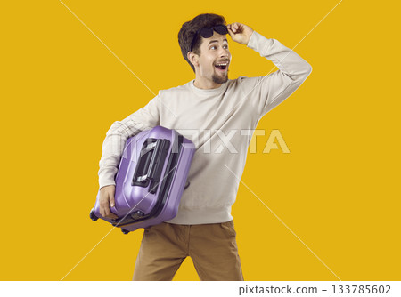 Happy man with purple suitcase looks away and smiles isolated on yellow background Happy man with purple suitcase looks away and smiles isolated on yellow background 133785602
