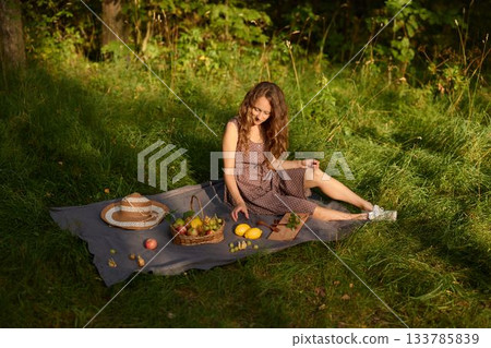 Bright young lady preparing fresh fruit on country blanket Bright young lady preparing fresh fruit on country blanket 133785839