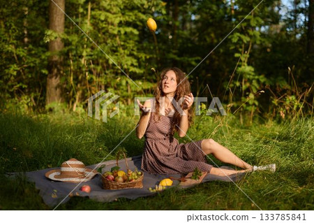 Cheerful young woman enjoys sunshine holding fruit outside 133785841