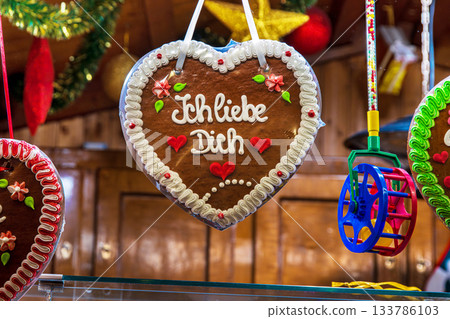 Lebkuchenherz decorated with the message Ich liebe dich hangs in a festive wooden stall. Romantic gingerbread heart at a traditional german christmas market 133786103