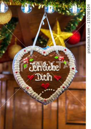 Lebkuchenherz decorated with the message Ich liebe dich hangs in a festive wooden stall. Romantic gingerbread heart at a traditional german christmas market 133786104