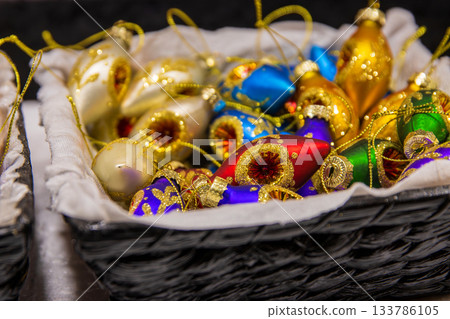Colorful handcrafted Christmas baubles in festive market basket. Vibrant handpainted Christmas baubles in a market basket, shining with gold, blue, green and purple 133786105