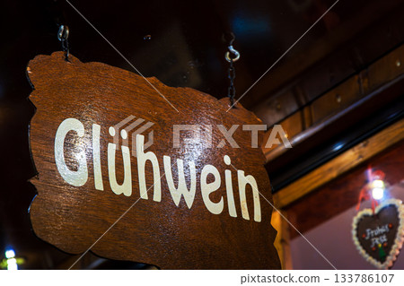 Rustic wooden sign Gluehwein in bright lettering hangs above a festive stall, inviting visitors to enjoy traditional mulled wine at a german christmas market 133786107