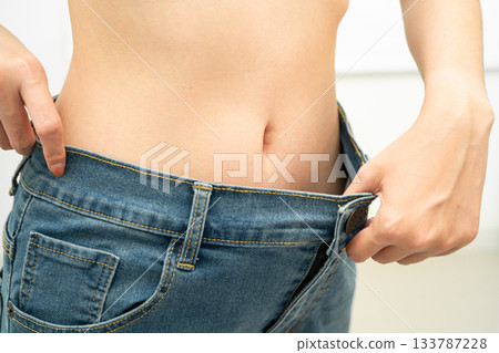 Young Asian woman losing weight wearing loose pants in oversize jeans. Young Asian woman losing weight wearing loose pants in oversize jeans. 133787228