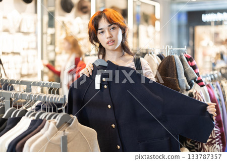 Young woman chooses coat in clothing store 133787357