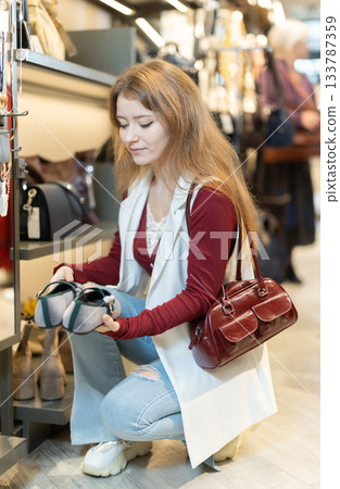 Positive young girl choosing shoes in clothing store Positive young girl choosing shoes in clothing store 133787359