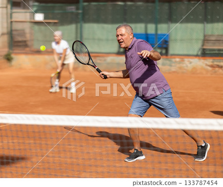 Elderly couple playing tennis together in court Elderly couple playing tennis together in court 133787454