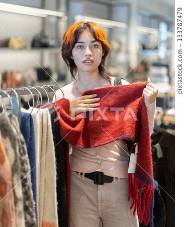 Attentive young girl choosing winter scarf in clothing store Attentive young girl choosing winter scarf in clothing store 133787479