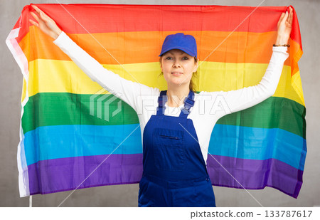 Cheerful female worker with wide grin on her face holding rainbow flag 133787617