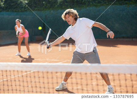 Couple of young paddle tennis players enjoying double match. Positive man training serving ball Couple of young paddle tennis players enjoying double match. Positive man training serving ball 133787695