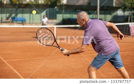 Rear view of focused european aged man playing tennis match in court of tennis club 133787757