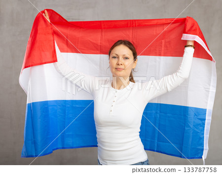 Smiling woman waving flag of Netherlands against gray background 133787758