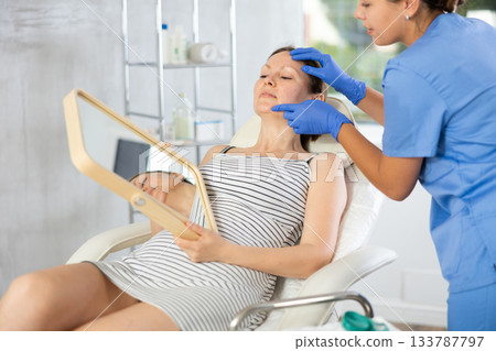 Woman cosmetologist examines patients face after lifting procedure and palpates chin area 133787797