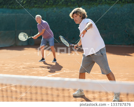 Sporty two men during doubles match on tennis court. Active sportsman hitting tennis ball with racket 133787876