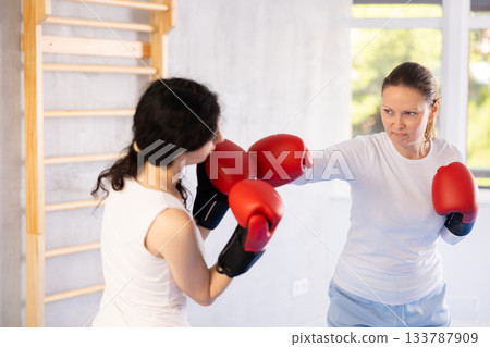 Focused woman practicing boxing punches in sparring during group self defence course 133787909
