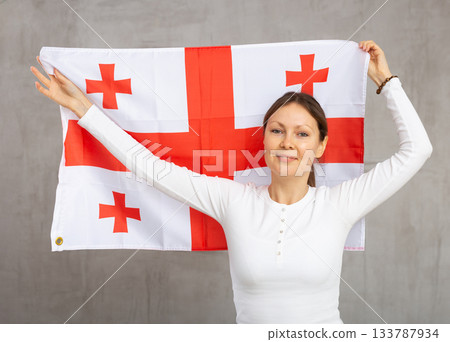 Happy young woman holding flag of Georgia against unicoloured background 133787934