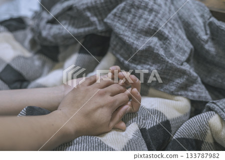Hands of two men holding hands on a blanket 133787982