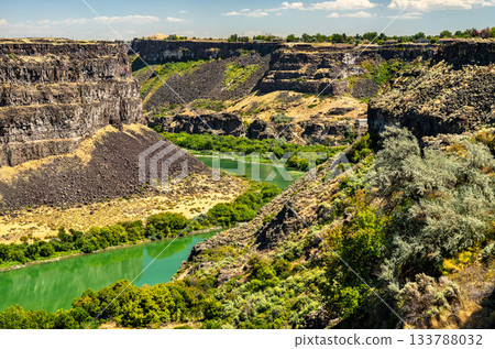 Green Snake River winds through rugged basalt cliffs of Snake River Canyon in Twin Falls, Idaho. Scenic landscape highlights dramatic geology of American West with contrast between arid canyon walls 133788032