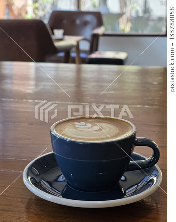 beautifully crafted coffee cup with latte art sits on wooden table, creating cozy atmosphere in cafe. background features blurred chairs, enhancing inviting vibe 133788058