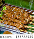 Close-up photo of chicken satay (sate ayam) on bamboo skewers, coated in peanut sauce and served on banana leaf 133788535