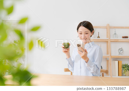 一位女士手捧綠色果汁和一部智慧型手機 一位女士手捧綠色果汁和一部智慧型手機 133788987