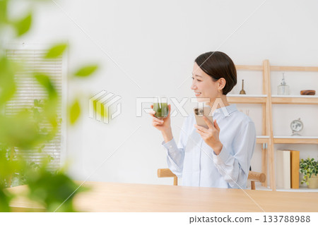一位女士手捧綠色果汁和一部智慧型手機 133788988